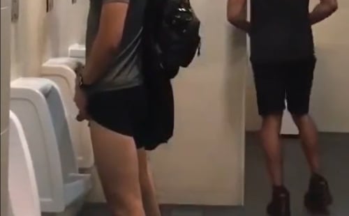 Jock pulls up shorts leg to piss at urinal